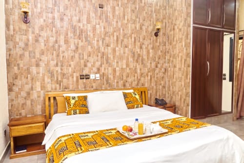 Suite moderne à l'Hôtel Yakro de Yamoussoukro avec carrelage mural, lit blanc, literie à motifs jaunes et bois foncé