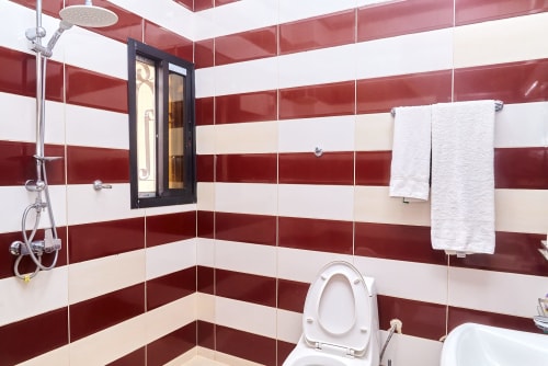 Salle de bain moderne de l'Hôtel Yakro avec carrelage rouge et blanc rayé, douche pluie, serviettes blanches et toilettes à Yamoussoukro