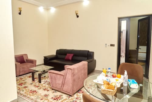 Suite à l'Hôtel Yakro à Yamoussoukro avec salon, canapé noir, chaises roses et coin repas