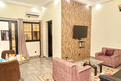 Suite de l'Hôtel Yakro à Yamoussoukro avec télévision écran plat, sièges roses, mur à carrelage et mobilier moderne.