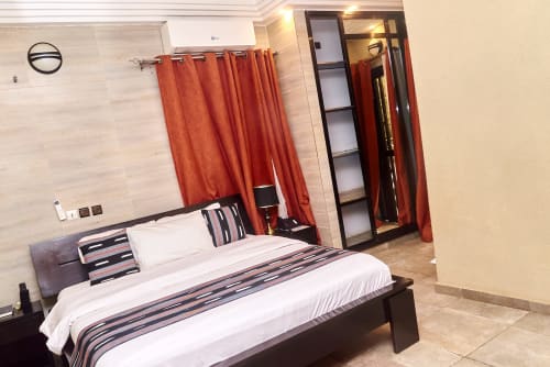 Suite moderne de l'Hôtel Yakro à Yamoussoukro avec lit queen, rideaux rouges et vue sur la ville