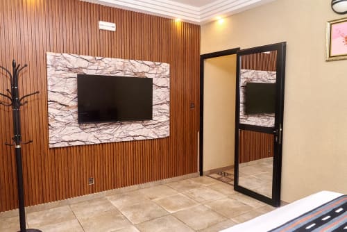 Suite de l'Hôtel Yakro à Yamoussoukro avec téléviseur écran plat, murs lambrisés en bois et élégant dosseret en marbre moderne