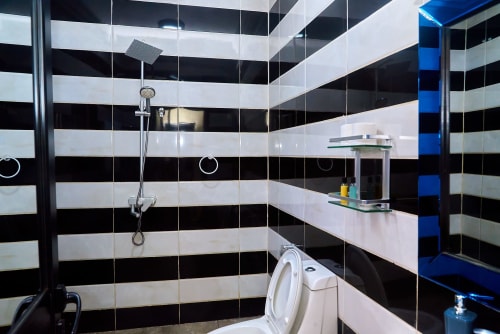 Salle de bains moderne aux murs carrelés noir et blanc rayé, douche, toilettes et lavabo à l'Hôtel Yakro de Yamoussoukro