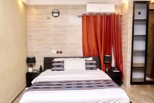 Suite moderne à l'Hôtel Yakro à Yamoussoukro avec lit queen, rideaux rouges et vue sur la ville