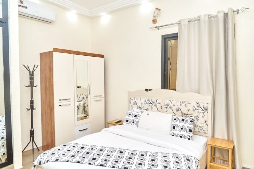 Chambre moderne à l'Hôtel Yakro à Yamoussoukro avec lit blanc, literie florale, armoire en bois et rideaux crème