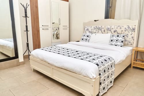 Chambre spacieuse à l'Hôtel Yakro à Yamoussoukro avec lit crème, draps blancs, tête de lit motifs et mobilier moderne
