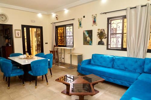 Salon moderne de l'Hôtel Yakro à Yamoussoukro avec canapés bleus, espace repas et œuvres d'art
