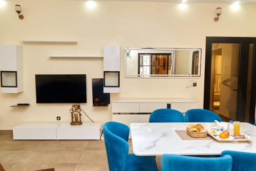 Salle à manger moderne avec chaises bleues, table en marbre et TV écran plat à l'appartement Hôtel Yakro de Yamoussoukro