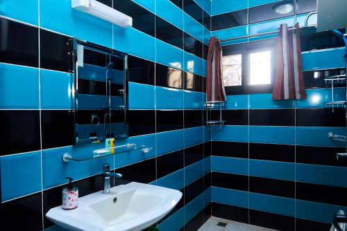 Salle de bains moderne de l'Hôtel Yakro avec carrelage rayé turquoise et noir, lavabo blanc, miroir et lumière naturelle