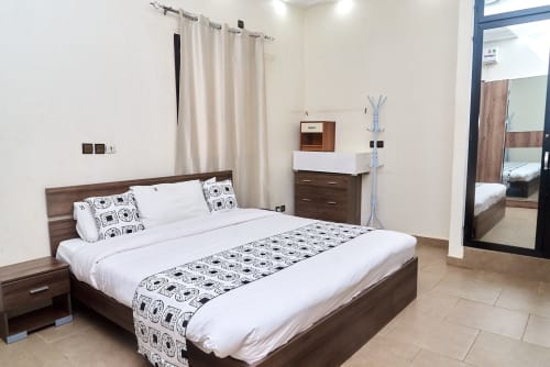 Chambre moderne à l'Hôtel Yakro Yamoussoukro avec lit queen-size, mobilier en bois foncé, linge blanc et plaid à motifs