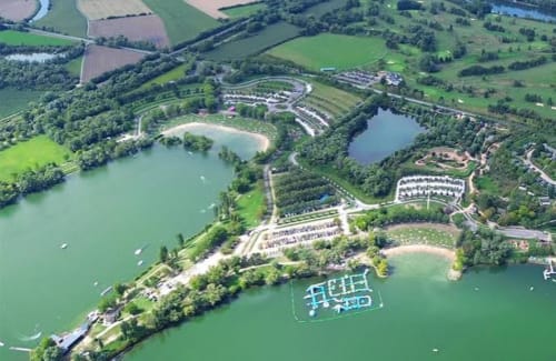 Vue aérienne du resort Les Gites De Flaubert au Héron, France avec lac turquoise, hébergements, parking et verdure luxuriante