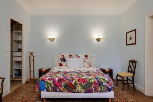 Chambre lumineuse du gîte Les Petits Toits avec parure florale colorée, mobilier en bois et appliques murales à Galgon, France