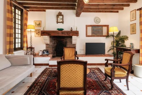 Salon rustique de la maison Les Petits Toits avec cheminée, poutres en bois, mobilier d'époque et tapis orientaux.