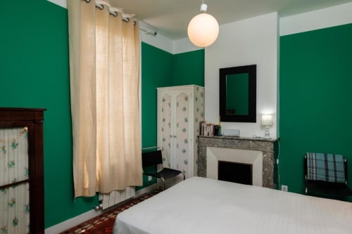 Chambre verte du gîte Les Petits Toits à Galgon, avec cheminée, rideaux crème et luminaire suspendu