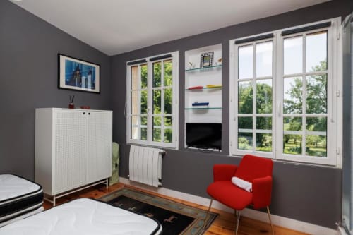Chambre moderne au gîte Les Petits Toits à Galgon avec fauteuil rouge, meuble blanc et vue sur jardin