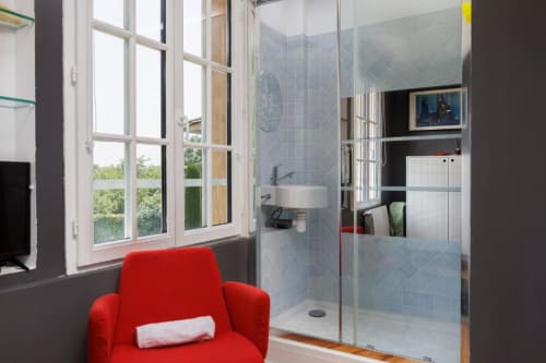 Salle de bains attenante moderne avec douche carrelage bleu, paroi vitrée et fauteuil rouge au cottage Les Petits Toits à Galgon