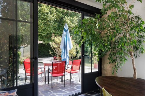 Terrasse de la cottage Les Petits Toits avec chaises rouges, parasol bleu et verdure luxuriante à Galgon