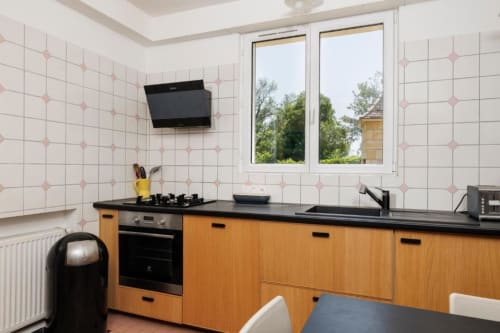 Cuisine moderne aux armoires en bois, plan de travail noir et murs carrelés roses de la maison d'hôtes Les Petits Toits à Galgon