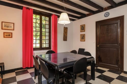 Salle à manger de la maison Le Clos de la Chapelle à Galgon avec table noire, rideaux rouges et plafond à poutres