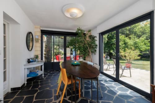 Salle à manger moderne du gîte Les Petits Toits avec table en bois foncé, chaises jaunes et vue sur la terrasse