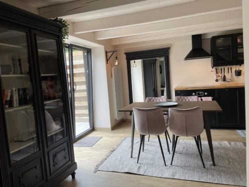 Salle à manger chaleureuse avec cuisine, table en bois, chaises rembourrées, placards noirs et portes donnant sur le jardin