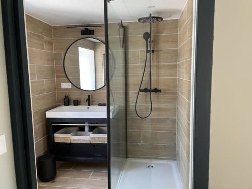 Salle de bain moderne du gîte Grand Saule avec murs en bois, miroir rond, lavabo blanc et douche ouverte