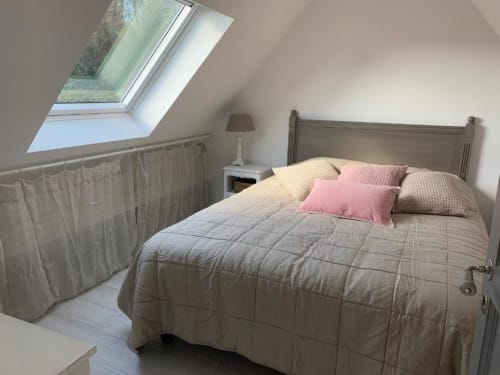 Chambre mansardée lumineuse aux Gîtes du Grand Saule avec puits de lumière, lit queen-size, coussins roses et vue sur le jardin
