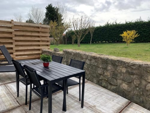 Table et chaises noires de salle à manger extérieure sur la terrasse avec mur en pierre du gîte Les gîtes du grand saule à Tardinghen