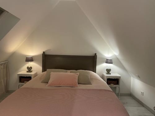 Chambre mansardée cozy aux Gîtes du Grand Saule à Tardinghen avec plafonds en pente, literie rose et deux tables de nuit