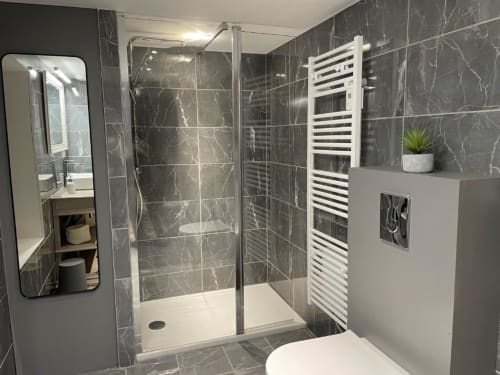 Salle de bain moderne aux carrelages en marbre noir, douche à l'italienne, radiateur-sèche-serviettes blanc et miroir de vanité aux Gîtes du Grand Saule