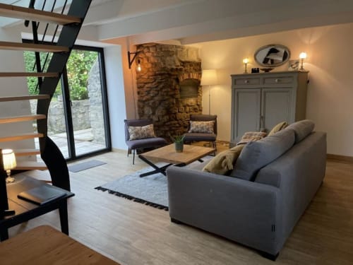 Séjour de gîte moderne avec canapé gris, cheminée en pierre et vue sur le jardin aux Gîtes du Grand Saule à Tardinghen