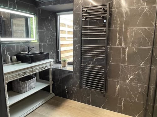 Salle de bain moderne aux Gîtes du Grand Saule avec carrelage marbre noir, vasque noire, sèche-serviettes chauffant et miroir LED