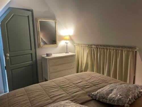 Chambre douillette aux gîtes du grand saule avec lit queen-size, commode en bois, miroir encadré et rideaux donnant sur le jardin