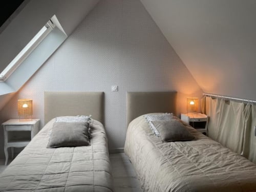 Lits jumeaux dans la chambre lumineuse du gîte en grenier aux Gîtes du Grand Saule, Tardinghen, avec puits de lumière et éclairage chaleureux