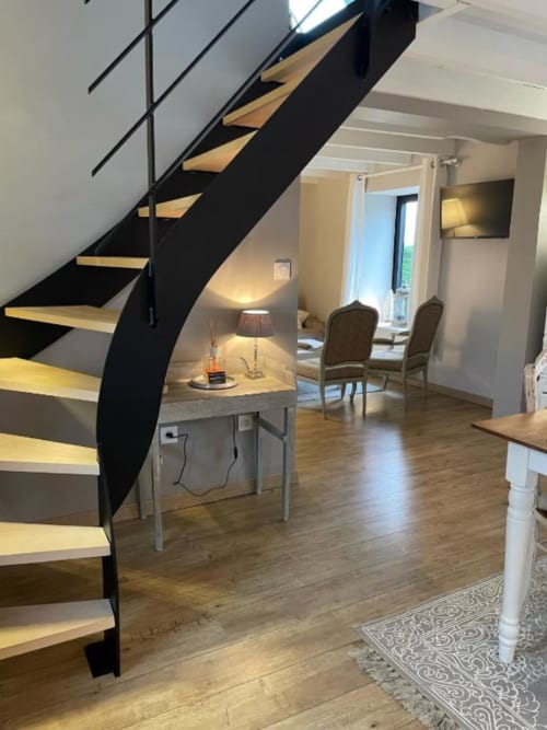 Intérieur de gîte moderne aux Gîtes du Grand Saule avec escalier hélicoïdal noir, parquet, bureau avec lampe et jardin