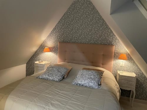 Chambre douillette sous les combles aux Gîtes du Grand Saule à Tardinghen : papier peint à motifs, tête de lit beige et touches d'orange