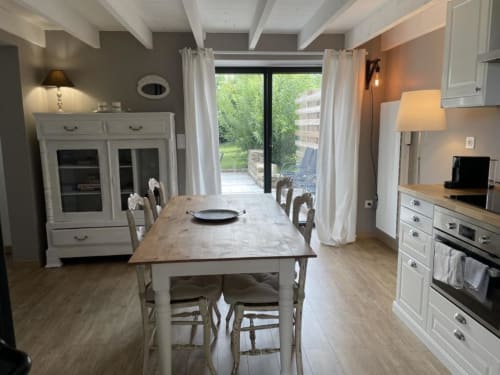 Cuisine-salle à manger de chalet moderne avec meubles blancs, table à diner et vue jardin par les grandes portes terrasse aux
