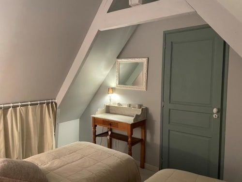 Chambre cosy avec plafond mansardé, coiffeuse en bois, porte verte et vue sur le jardin aux gîtes du grand saule