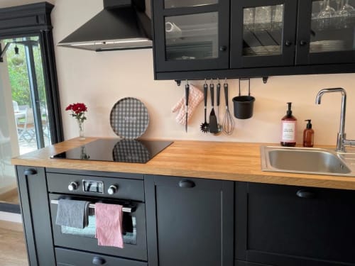 Cuisine cottage moderne aux armoires noires, comptoirs en bois, évier et appareils en acier inoxydable aux gîtes du grand