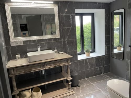 Salle de bain moderne avec carrelage en marbre, vasque design, élégante vanité, grands miroirs et vues sur le jardin aux Gîtes du Grand Saule