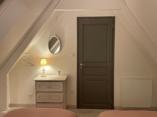 Chambre mansardée aux Gîtes du Grand Saule à Tardinghen : porte en bois foncé, miroir ovale et lampe de chevet