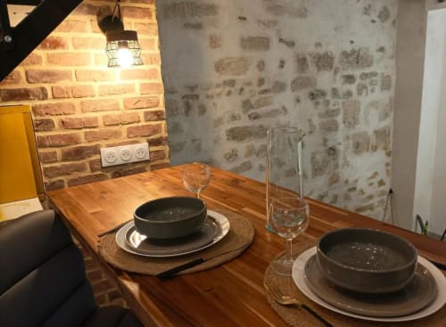 Table rustique au Loft Le Travertin à Avignon, dressée pour deux avec bols foncés et verres, murs en pierre et briques apparentes.
