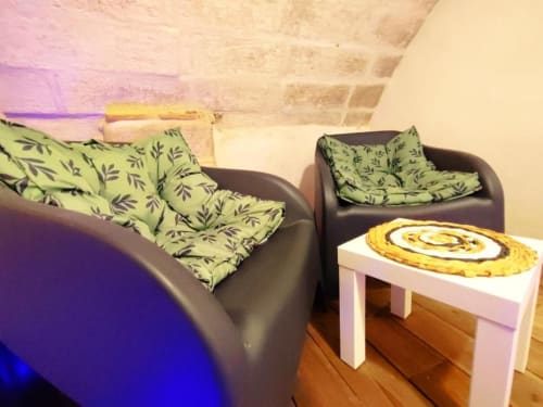 Salon du Travertin Loft avec fauteuils en cuir noir, coussins motif vert, table d'appoint blanche et œuvres d'art colorées