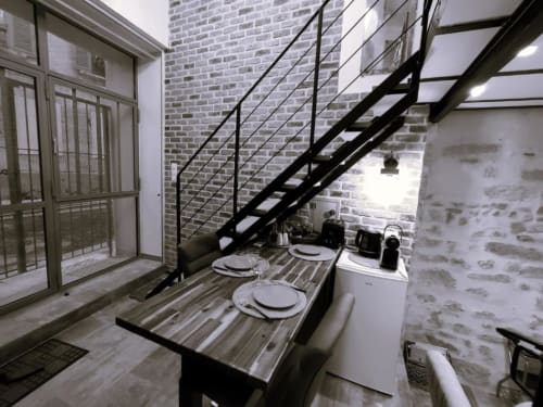 Cuisine-salle à manger du Travertin Loft avec murs en brique, escalier en métal noir, table dressée et électroménagers modernes à Avignon