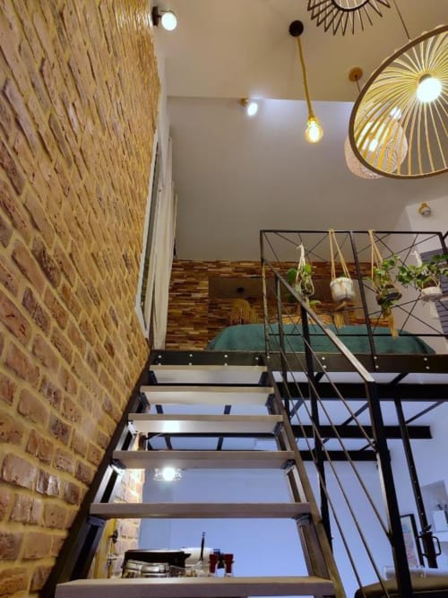 Escalier loft moderne dans un appartement avignonnais avec briques apparentes, luminaires suspendus et plantes en pot sur rampes métalliques