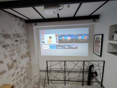 Salon du Travertin Loft avec écran de projection affichant les services de streaming, mobilier moderne et murs en pierre