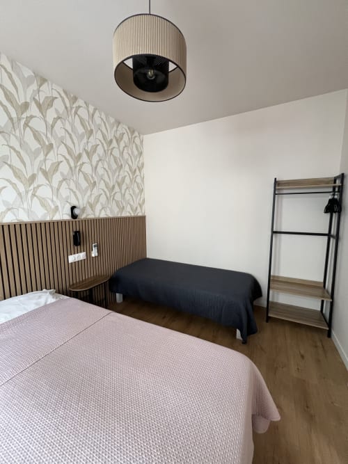 Chambre moderne de l'Hôtel Les Paquebots à Port-Vendres avec lit rose, tête de lit en bois, suspension noire et étagères métalliques