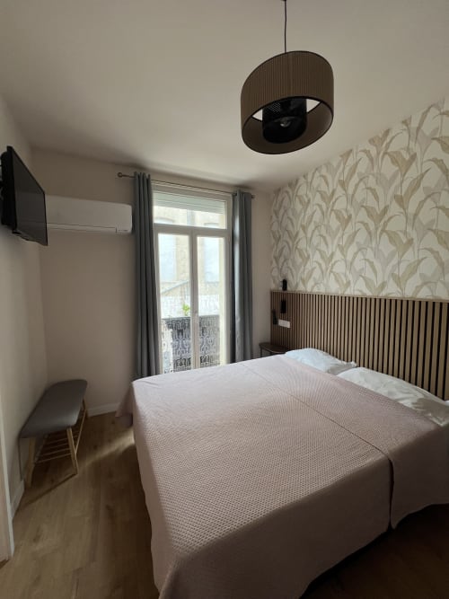Chambre d'hôtel moderne aux Paquebots avec lit double, portes-fenêtres, lampe suspendue et papier peint botanique