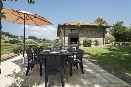 Pátio da Quinta de Carvalhal com mesa de refeições, guarda-sóis e vistas da paisagem rural em Guimarães