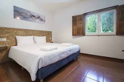 Quarto aconchegante e iluminado na Quinta de Carvalhal com cama king, cabeceira de cortiça, piso em terracota e vista para o jardim